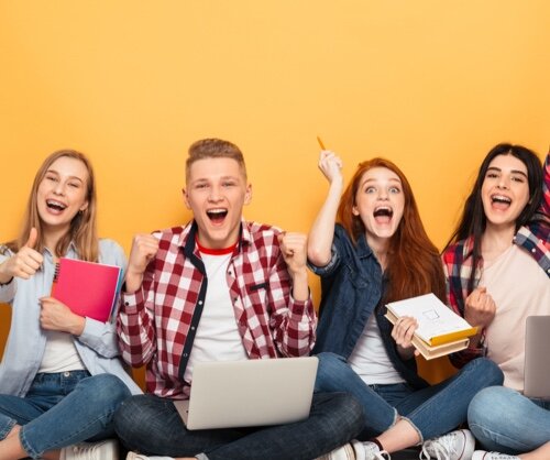 Junge Leute feiern Zusammengehörigkeit Gruppe von fröhlichen Schülern, die auf dem Boden sitzen und lächeln. Sie halten Bücher und einen Laptop, während sie ihre Freude über ein Ereignis teilen. Der Hintergrund ist gelb.